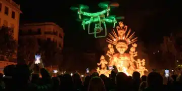 Dron con luces verdes sobre una multitud observando una falla valenciana por la noche, simbolizando la fusión de tradición y tecnología en la cultura española digital.