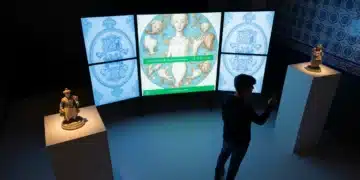Persona en un espacio de exhibición digital observando una pantalla con detalles de arte clásico español, con elementos de cerámica tradicional en primer plano, representando la fusión de lo digital y la cultura.