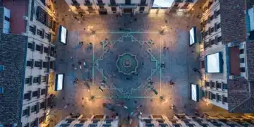 Vista aérea de una plaza histórica española al anochecer, con luces tradicionales y detalles modernos en tonos verdes, mostrando la fusión de cultura y tecnología.